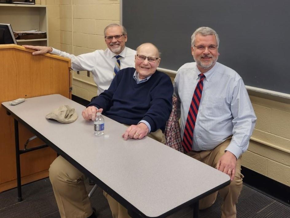 Three men in a classroom, smiling at the camera.