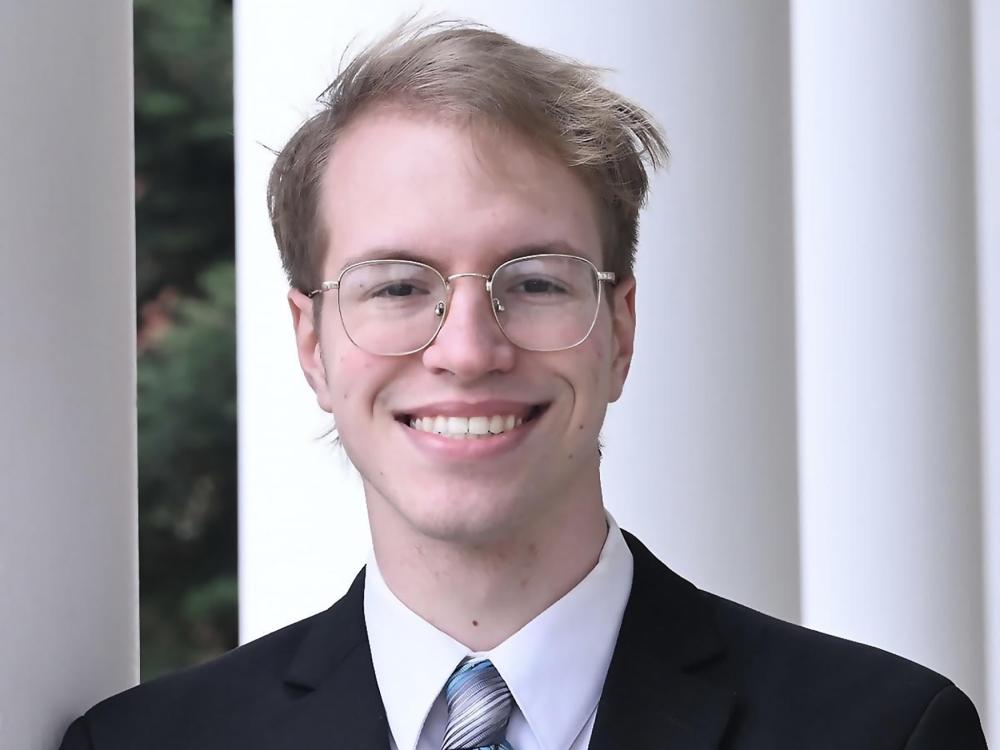 Smiling blond haired main wearing round glasses and a coat and tie