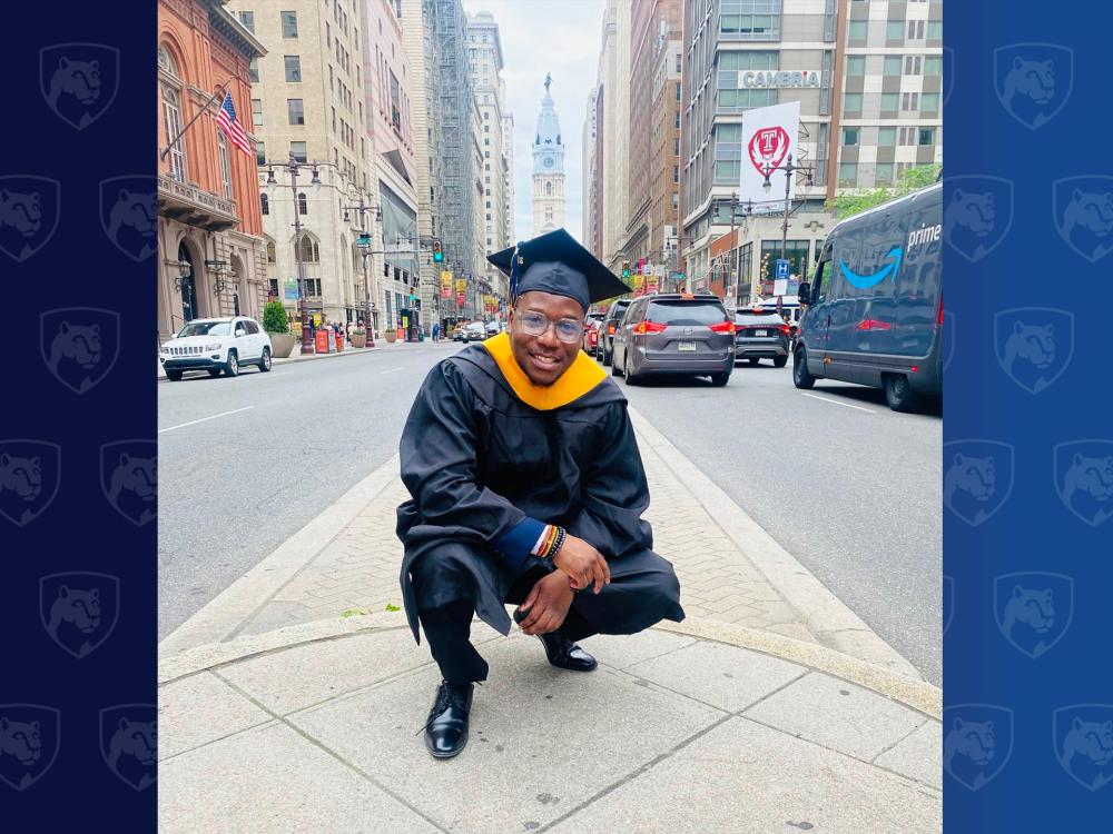 Man in cap and gown crouching near City Hall in Philadelphia