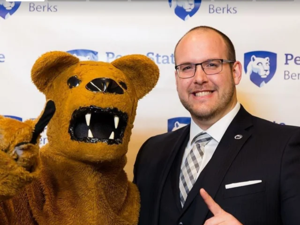 A person stands with the Nittany Lion, both hold up their index fingers
