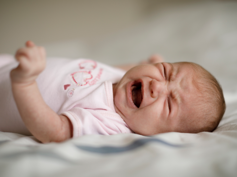 Newborn baby laying down and crying.