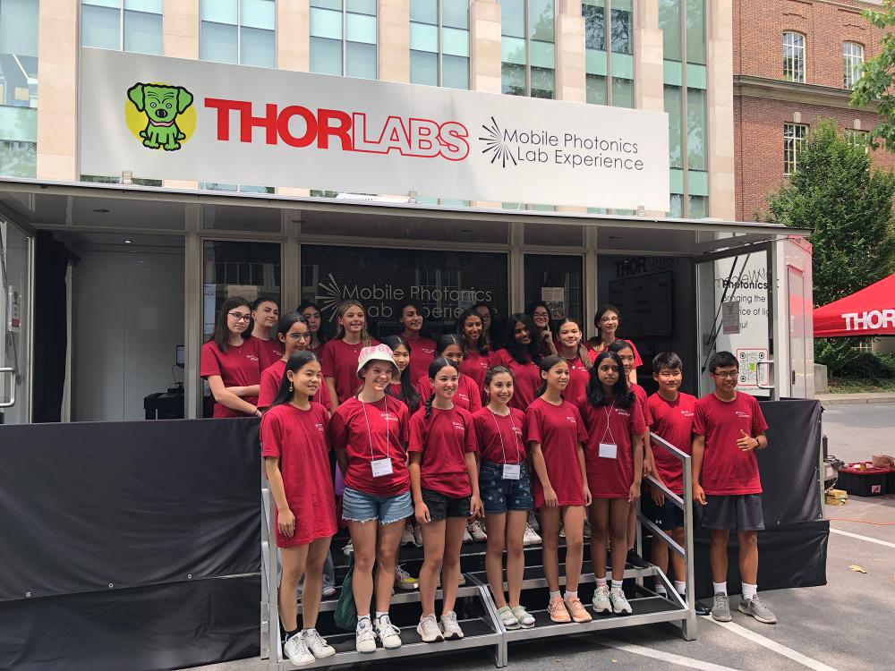 Group of people in red shirts stand under a banner reading "THORLABS"