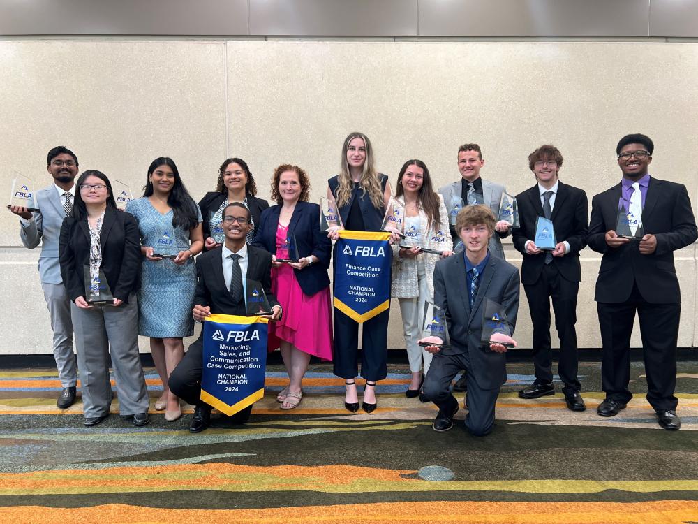 A group of students stand with a faculty member, showing off awards.