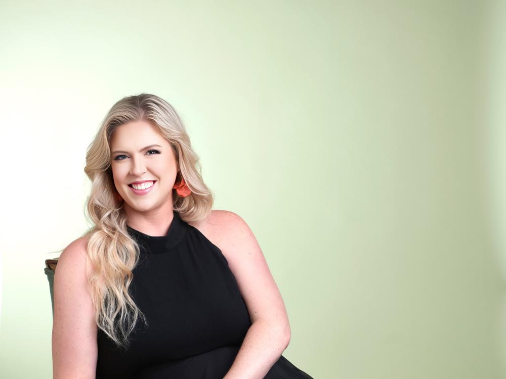 Blond woman with black dress sitting casually on a green lounge chair smiling