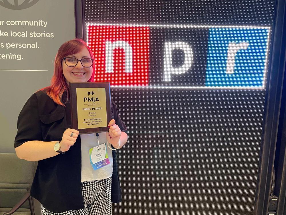 Women photographed with award in front of an NPR sign.