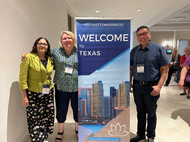 Three people smile in front of a banner