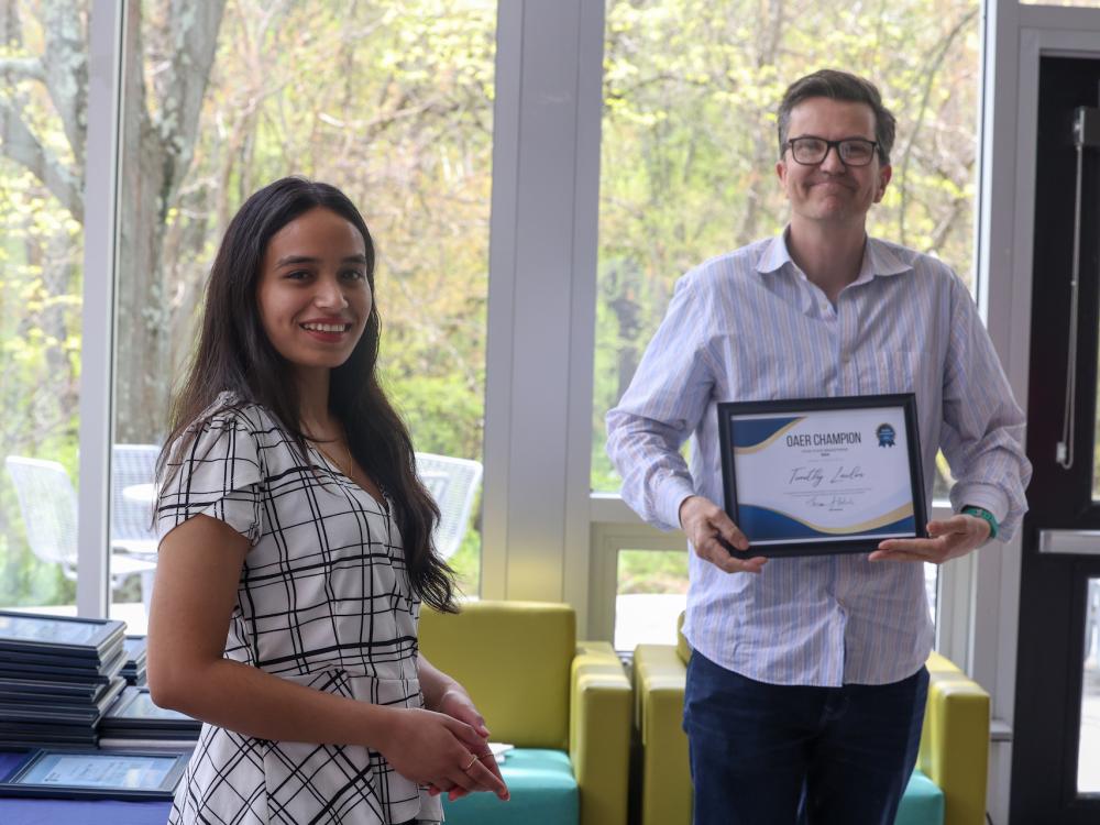 Two people stand with a framed certificate 