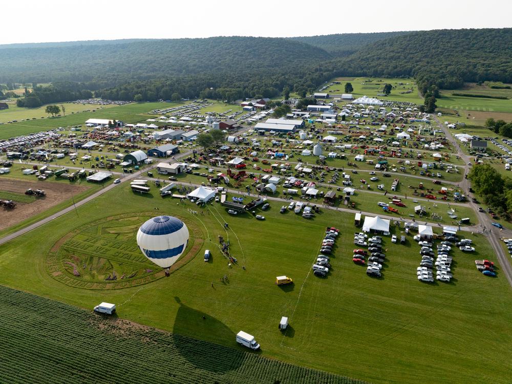 A hot air balloon floats over a field of people and parked vehicles