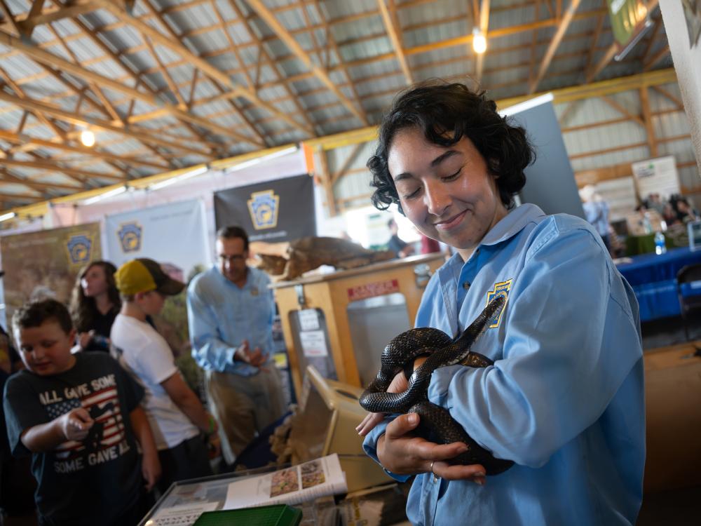 An individual in a blue shirt holds a small snake up toward the camera.