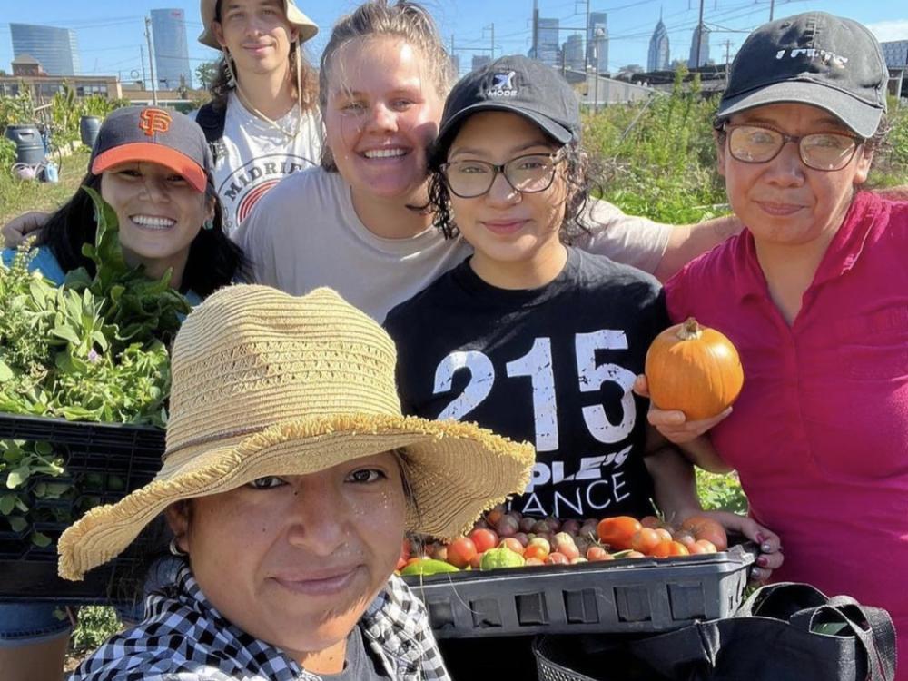 People smiling, grouped together holding vegetables on a sunny day