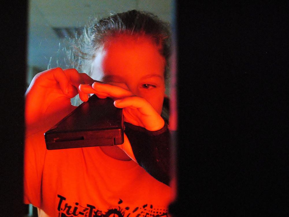 A girl looks through a light spectrum during a science experiment.