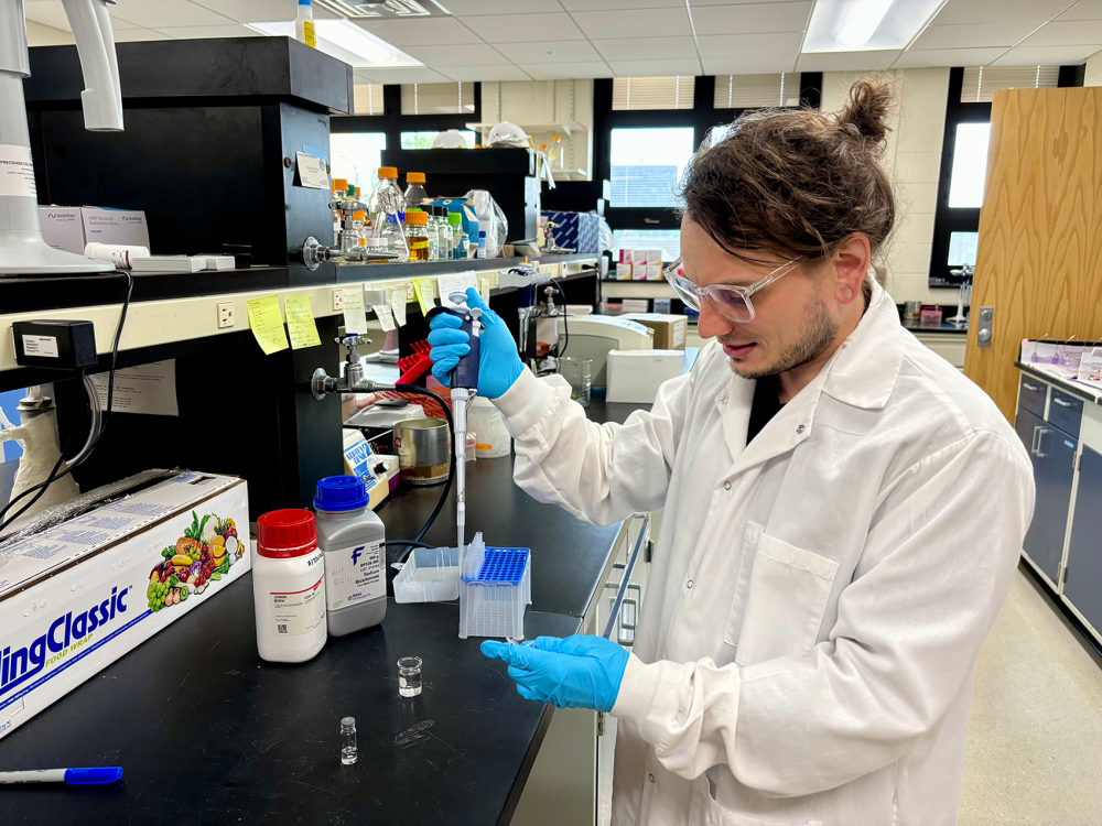 Scientist in white lab coat pipetting fluid into a vial