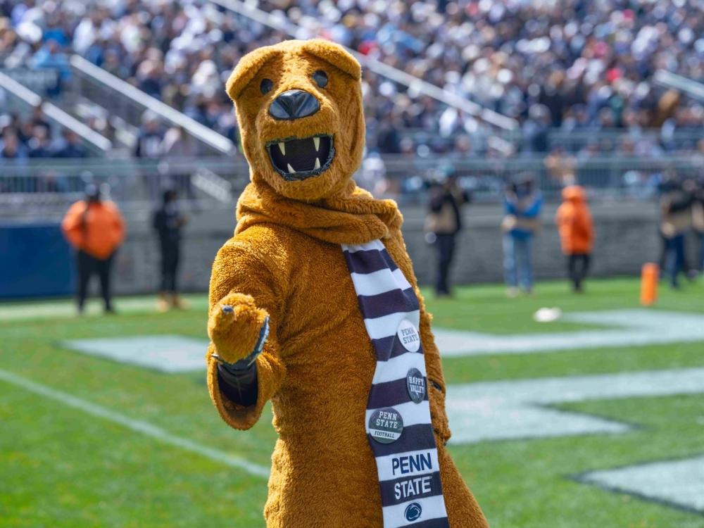 The Nittany Lion points to the camera while standing on the football field