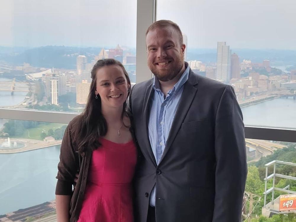 A man and woman stand in front of a window overlooking downtown Pittsburgh.