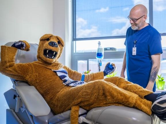 The Nittany Lion sits on a medical bed flexing his arm after donating blood