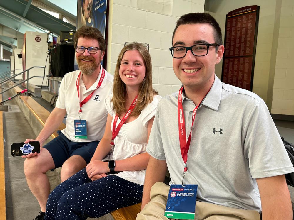 Three people seated on a bleacher seat and smiling at the camera