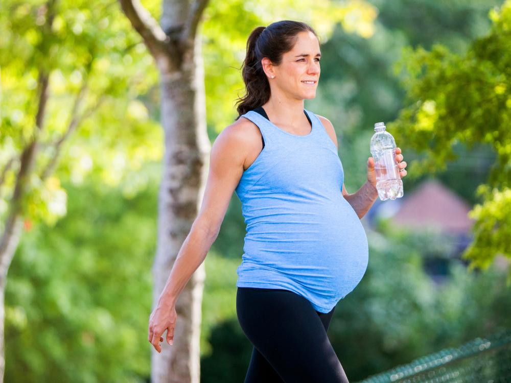 Pregnant woman walking outside carrying a bottle of water