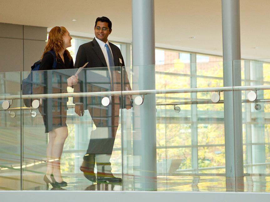 A photo of two students, one male and one female, walking on the bridge in the Business Building.