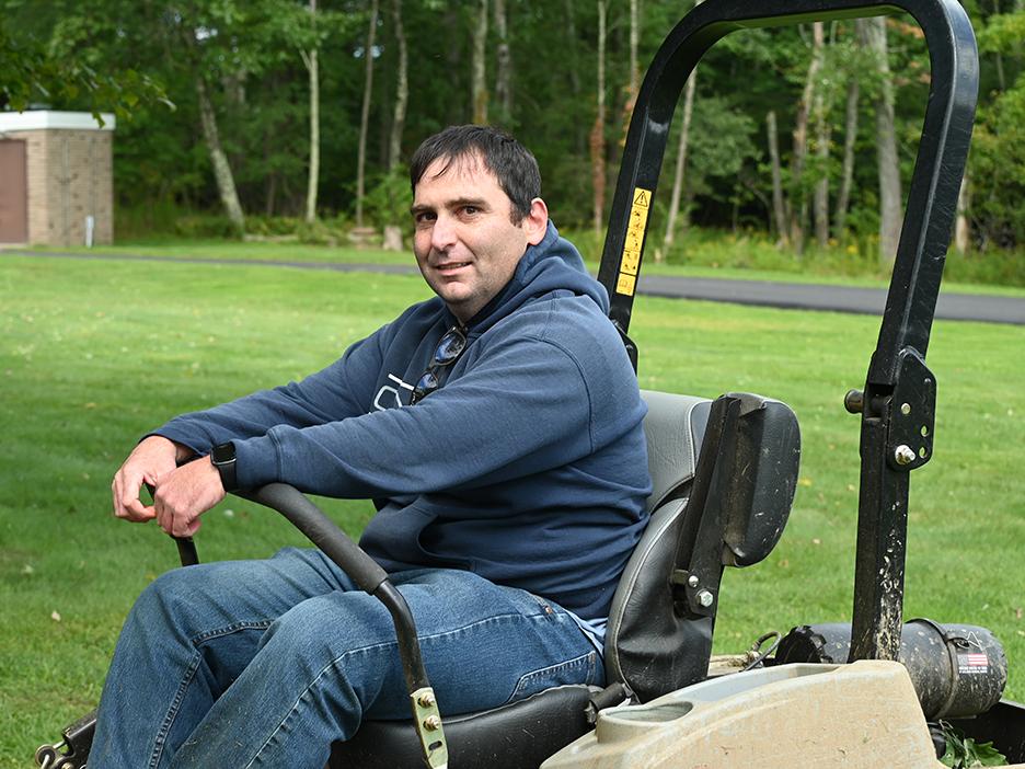 A man sitting on a riding lawn mower with the lawn behind him.