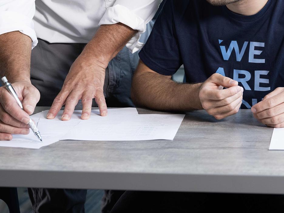 A close-up of the hands of an instructor writing on a sheet of paper next to the hands of a student seated alongside.
