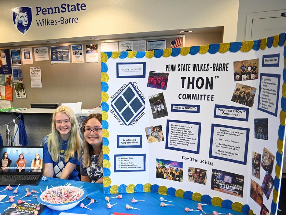 Two women at a table sitting next to a posterboard promoting the campus' THON organization.