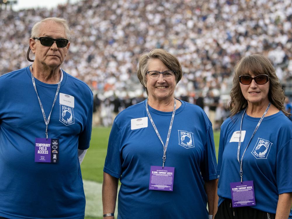 Three people stand on a football field in a crowded stadium.