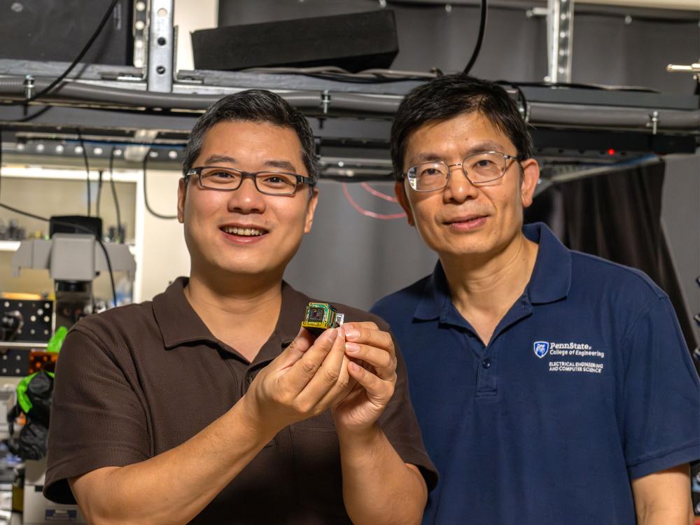 Two individuals pose in a lab holding a small device known as a metasurface. 