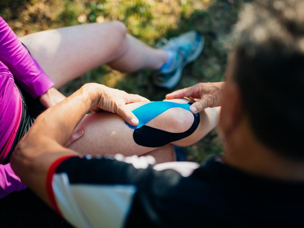 A man applies a bandage on knee of his wife.