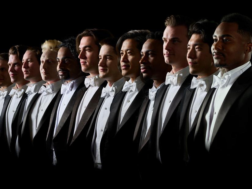 A group twelve diverse me wearing tuxedos stand and look in the same direction.