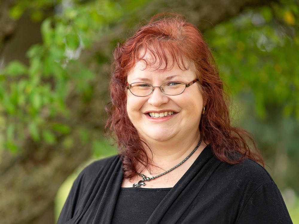 A photo of Gill taken outside. She is smiling and wearing a black jacket.
