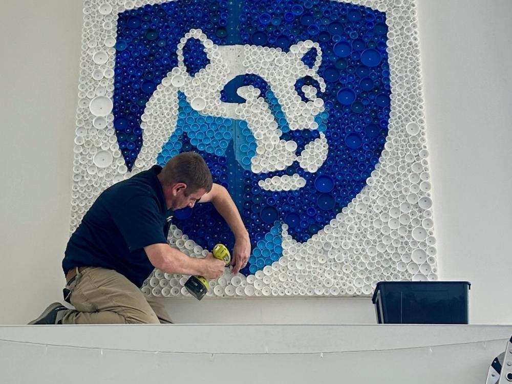 A person uses a drill to install a Nittany Lion mural