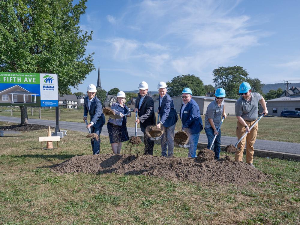 A group of people with shovels participate in an outside groudbreaking ceremony on a beautiful summer day