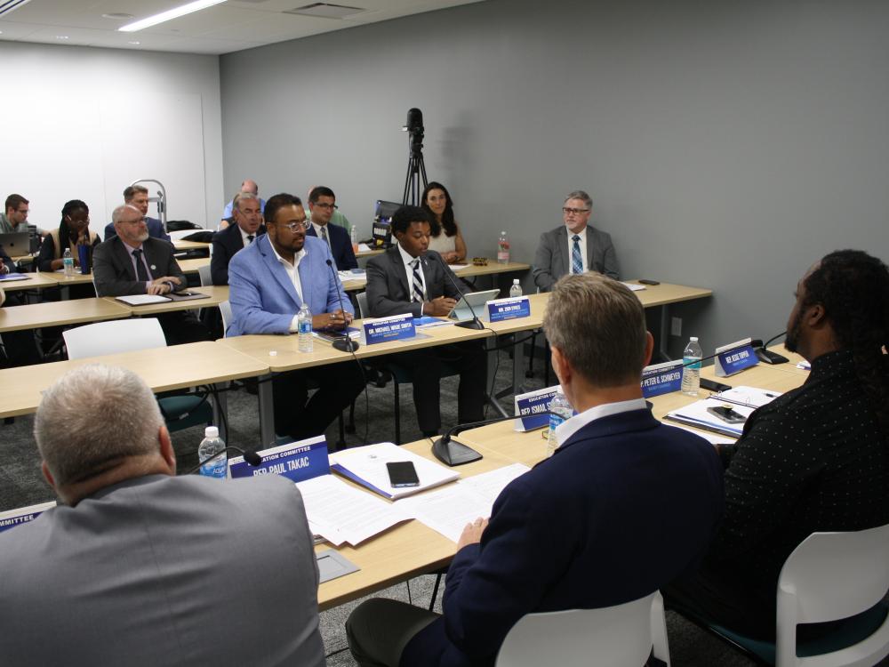 two men sitting behind a table infront of microphones infront of them speaking to a room full of people