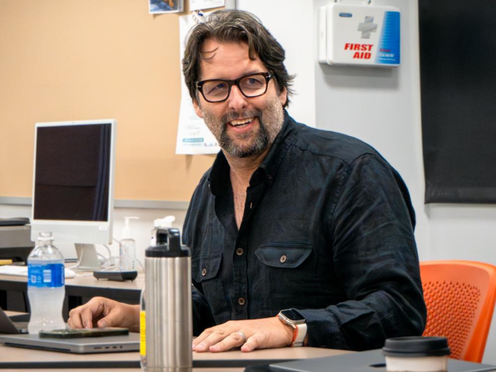 Michael McIntyre sits in a classroom while engaging with students. 