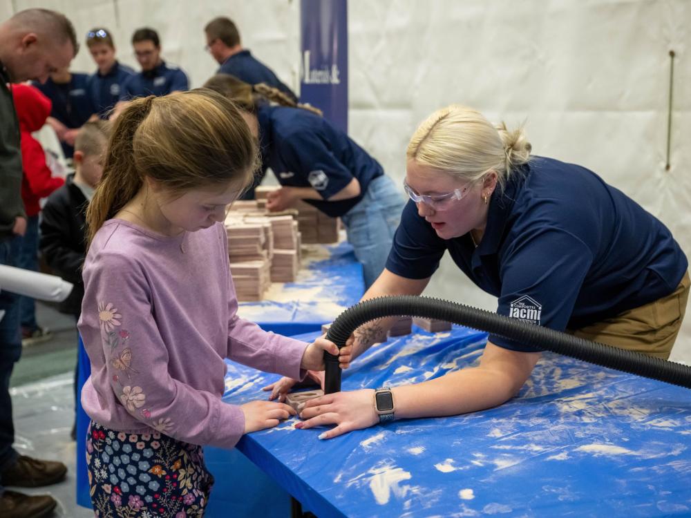 A volunteer helps a child clean out a sand mold used in metal-casting.
