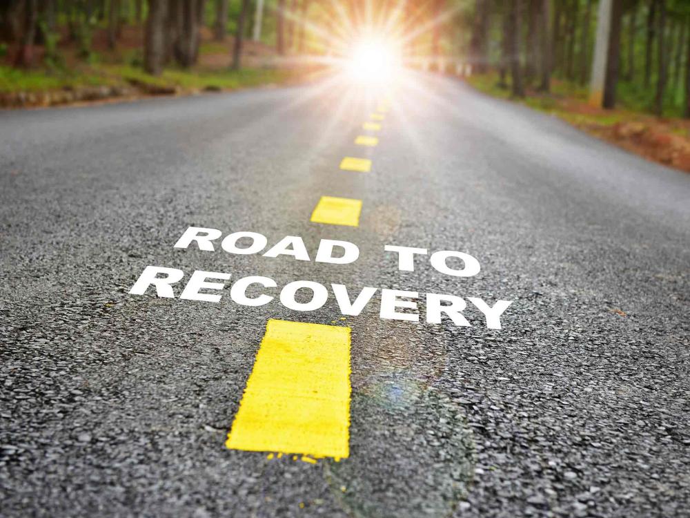 road that says road to recovery, leading to a bright sun in the distance