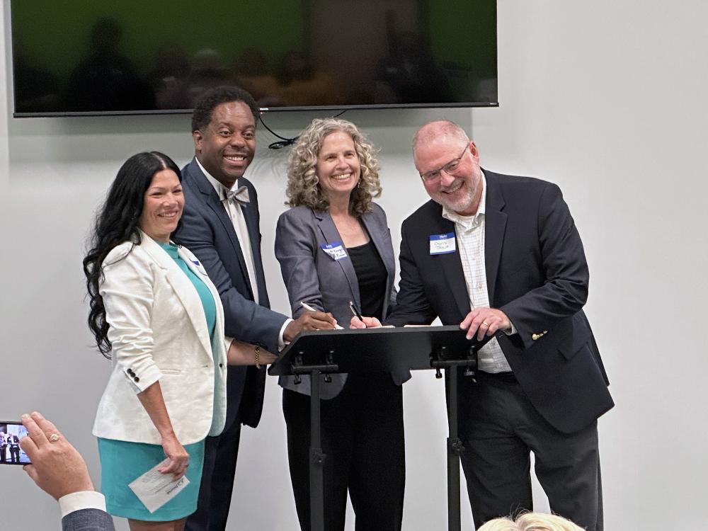 A group of four people, two men and two women, smile as they prepare to sign a document