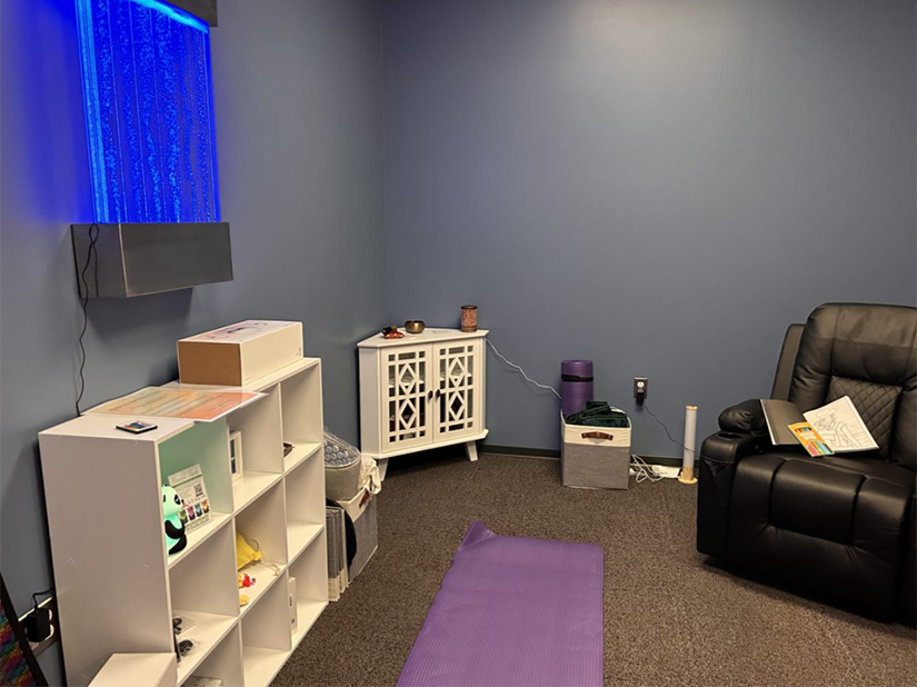 A room with blue walls, a white dresser on the left and a brown comfortable chair at right.