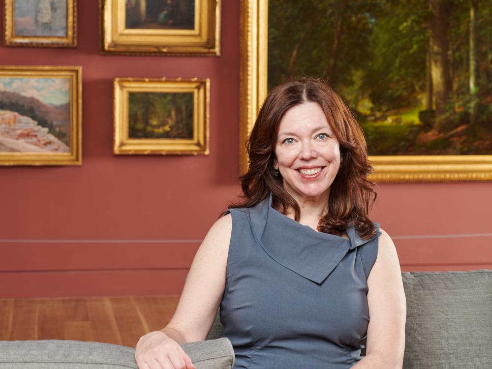 Woman with dark hair sitting on couch in front of a gallery wall