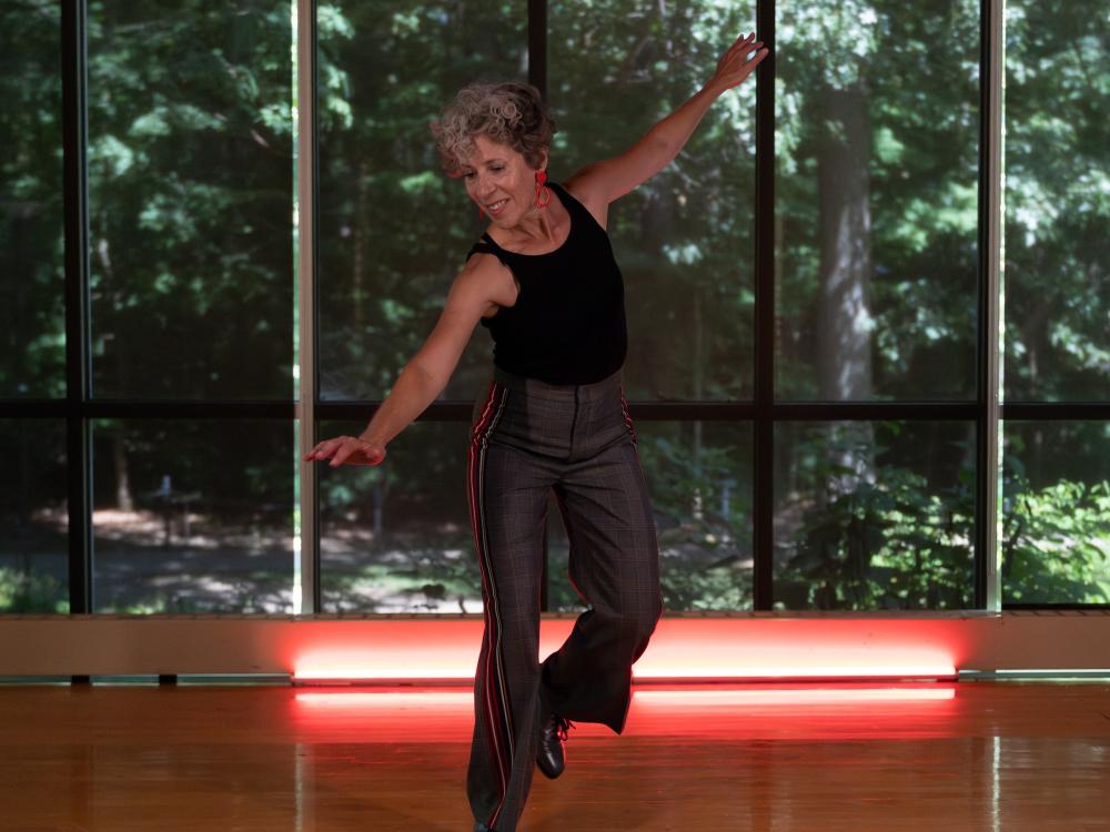 Woman tap dancing in a studio in front of wall of windows