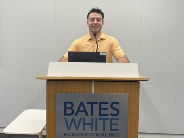 Colin Byrne stands behind a podium that reads Bates White Economic Consulting on the front.