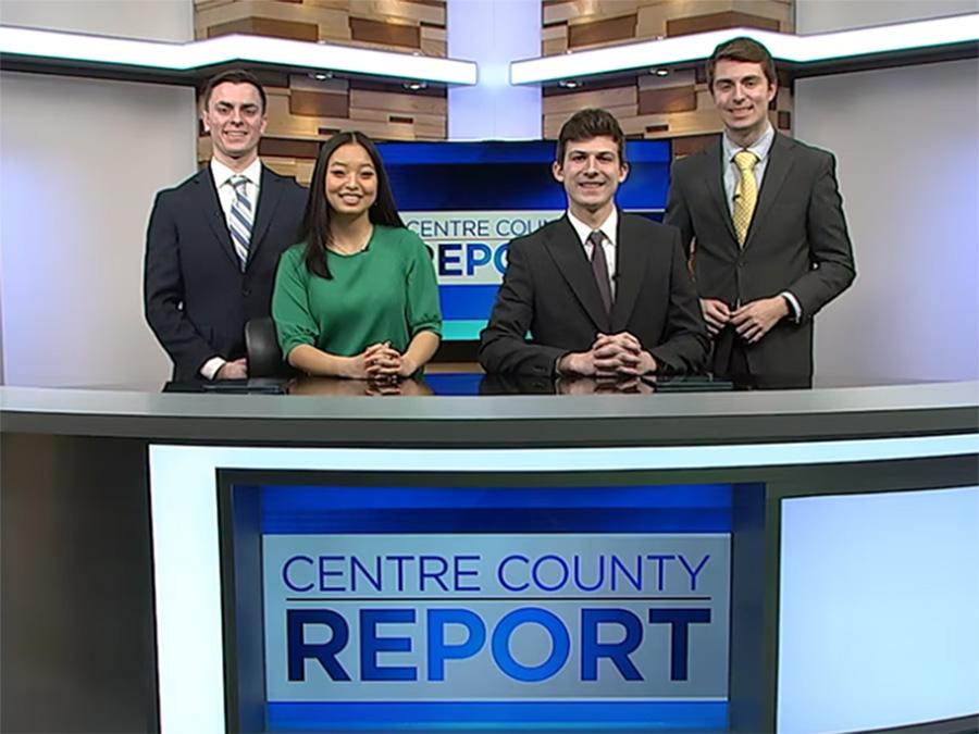 Four students stand behind a newsdesk