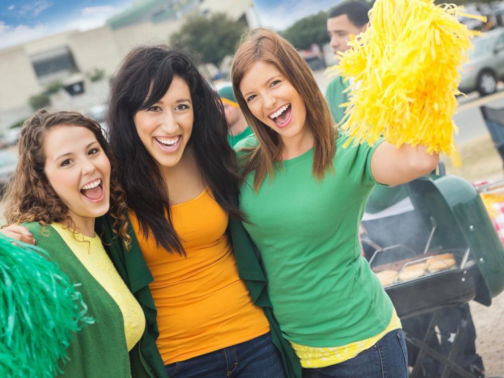 Three young people outside a sporting event wearing team colors and holding pom poms
