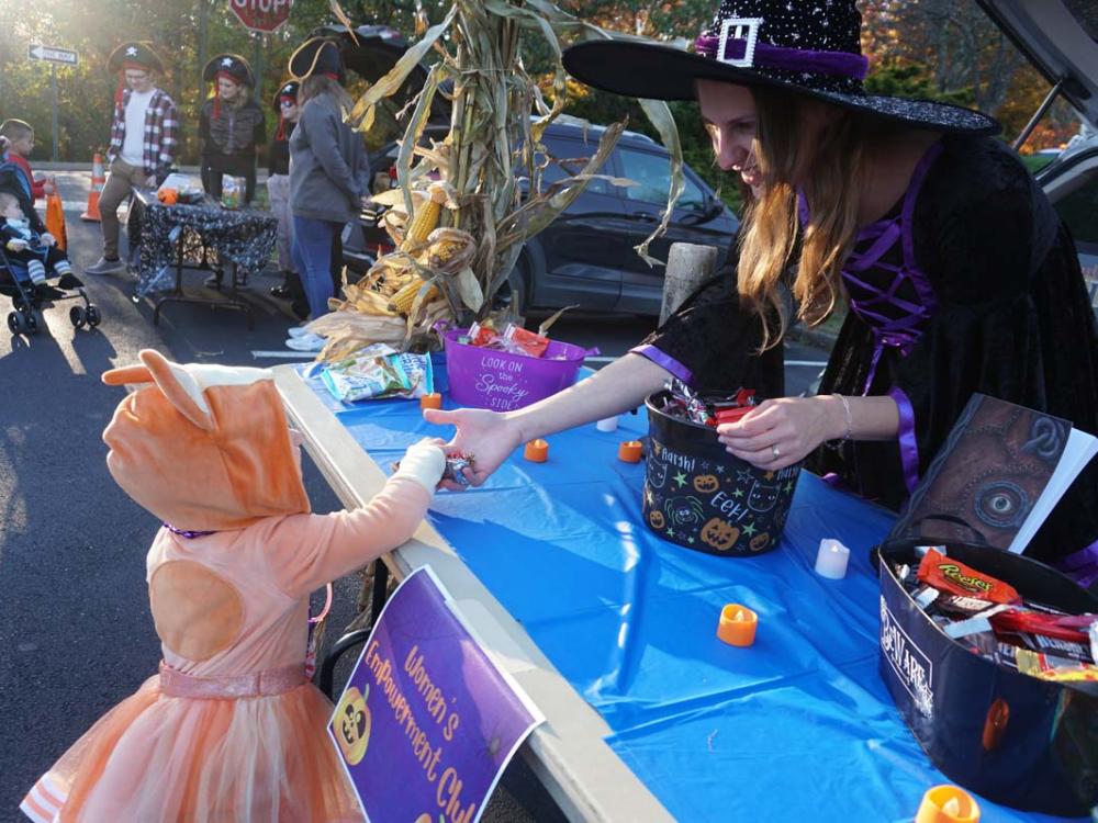 A Penn State Hazleton student dressed in a witch's costume hands candy to a young child dressed as Bingo from Bluey. 