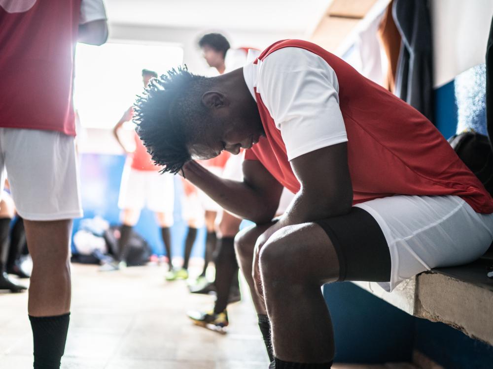 Male athlete in locker room holds his head and looks pained