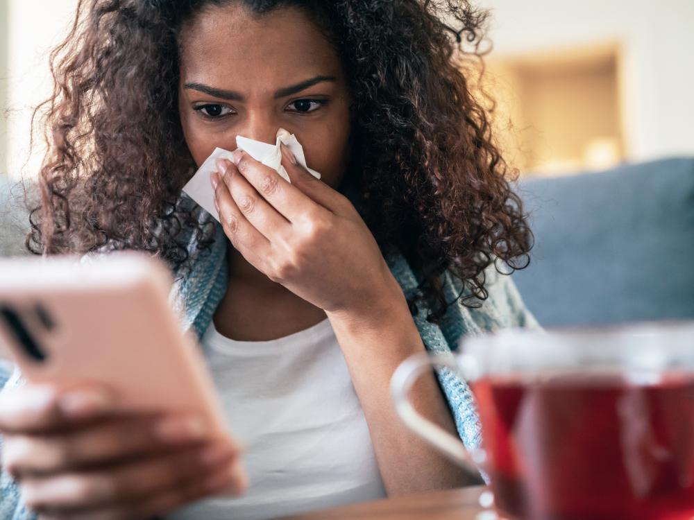 A person using their smartphone while blowing their nose with a tissue