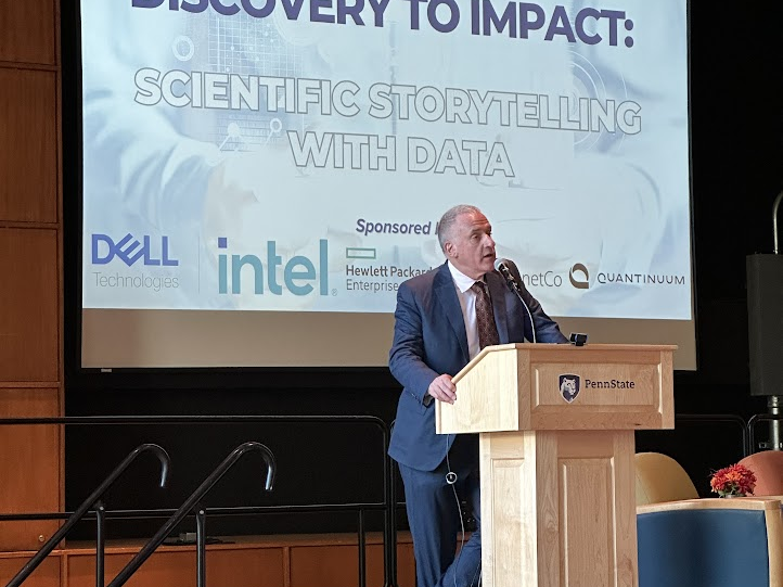 Andrew Read, Senior Vice President for Research, stands on stage at a wooden podium presenting opening remarks.