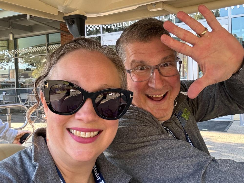 Family Weekend volunteers smile and wave while riding on a golf cart