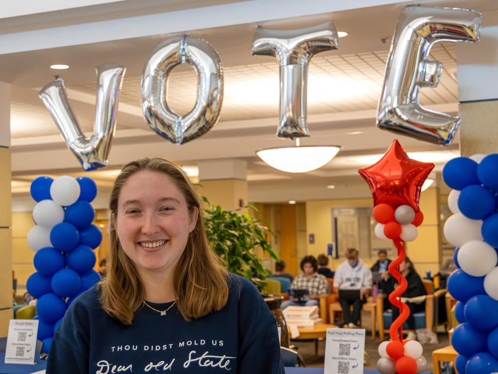 Maddie Hindman stands in front of a balloon arch spelling out “VOTE” in the HUB-Robeson Center.