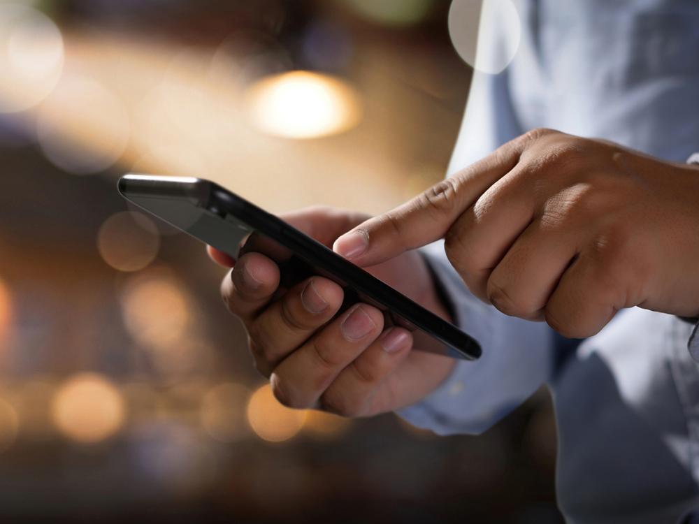 Hands holding a smart phone in front of a blurry background.